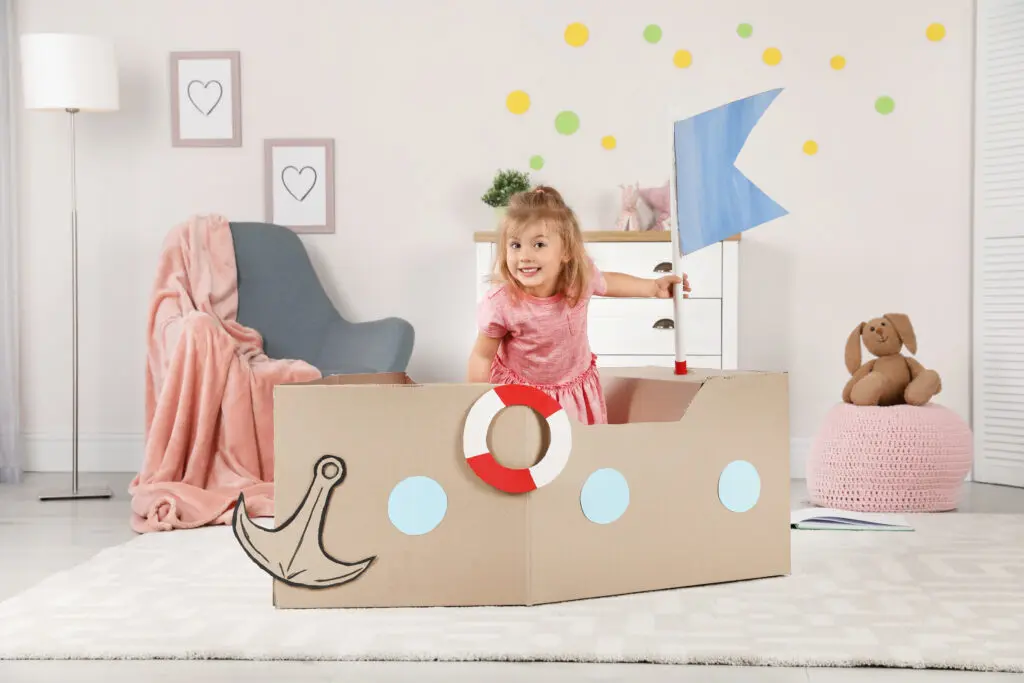 Cute little girl playing with cardboard ship at home