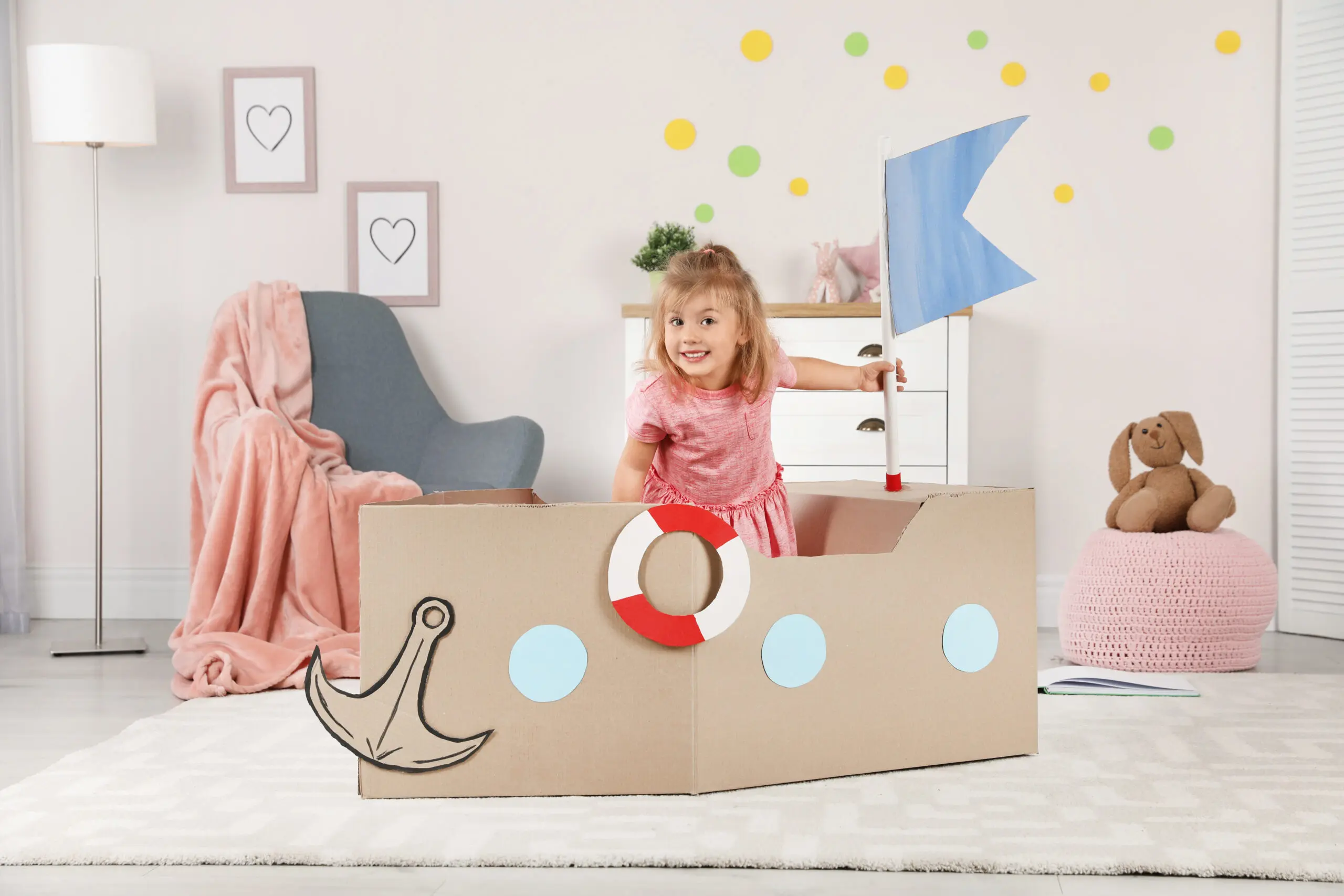 Cute little girl playing with cardboard ship at home